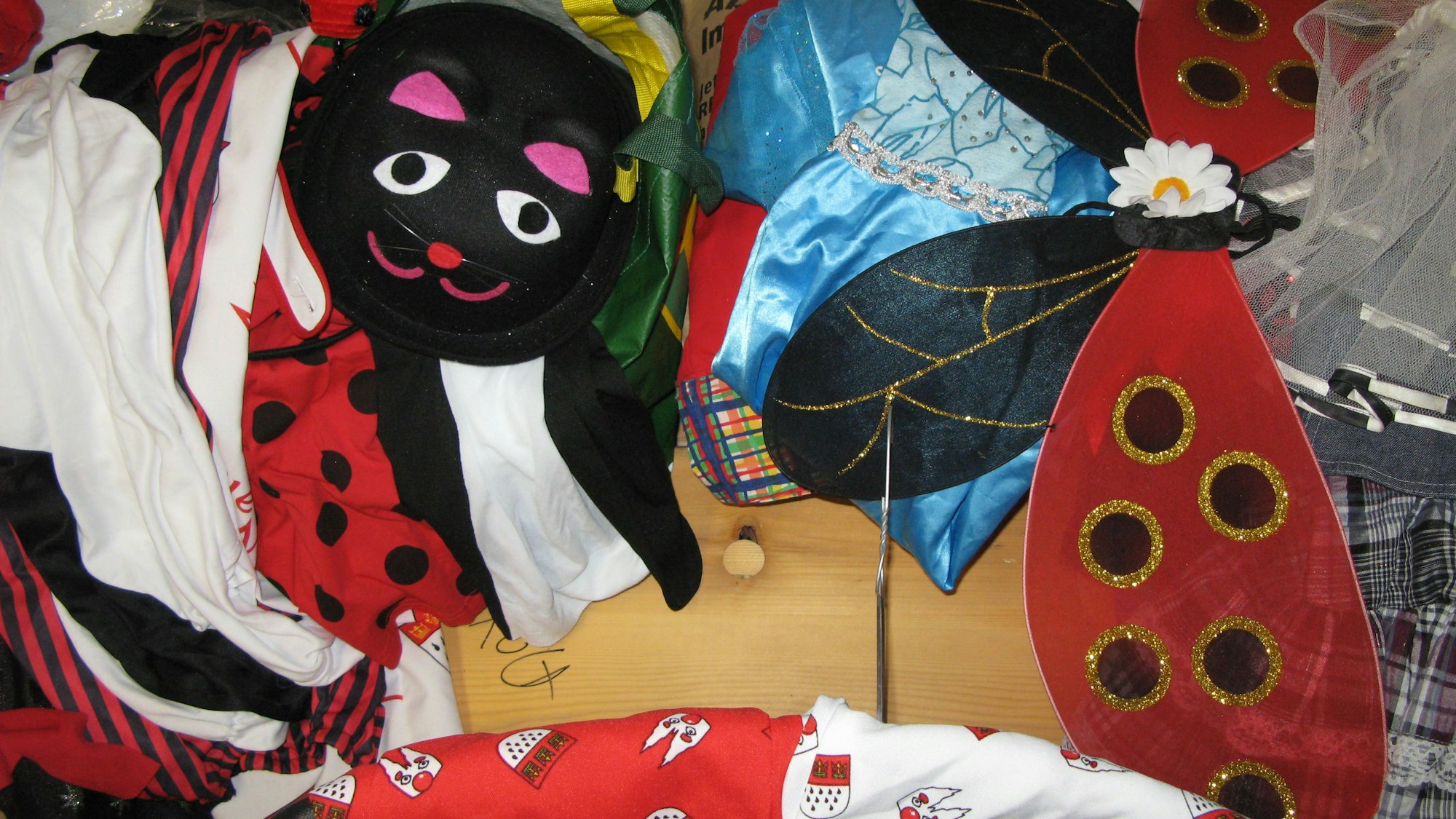 Kostümteile wie eine Katzenmaske und Schmetterlingsflügel liegen auf einem Tisch.