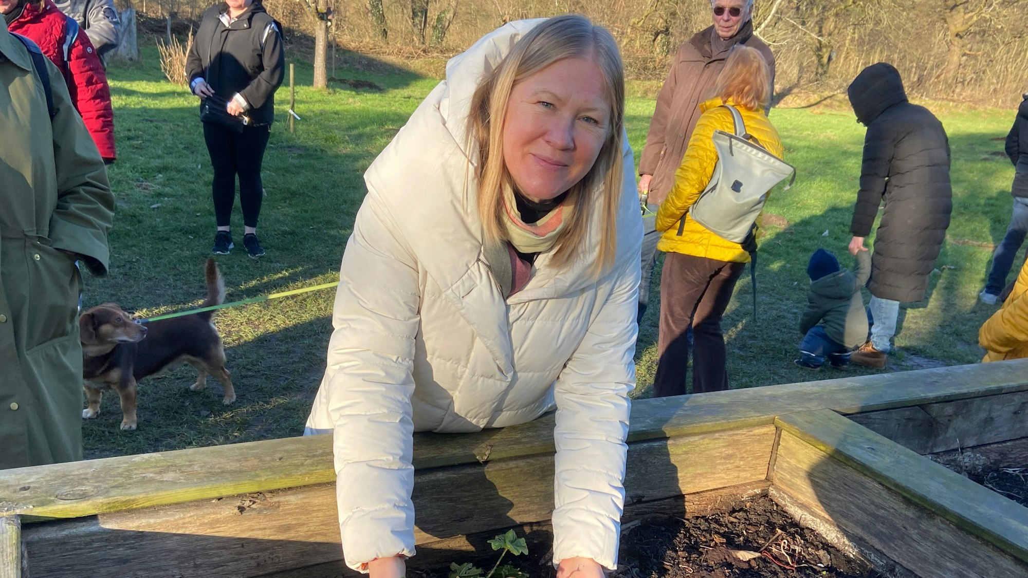 Eine Frau steht an einem Kräuter-Hochbeet und umfasst mit den Händen eine Pflanze.