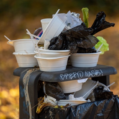 Benutze Einwegbehälter und Teller stapeln sich auf einem überfüllten Mülleimer in einem Park.
