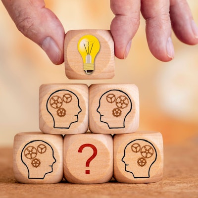 Mehrere Holzwürfel sind markiert mit Fragezeichen und ein Würfel mit der Lösung wird von einer Hand darüber gehalten