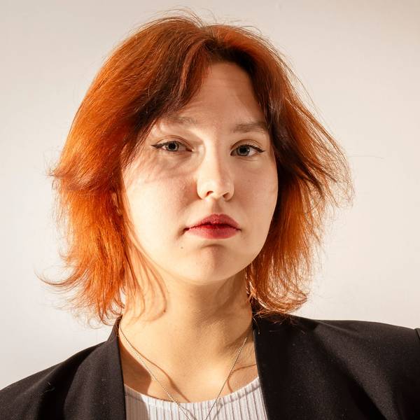 Katharina Zenses
ist im Porträt zu sehen. Sie hat gestuftes rotes Haar und blickt in ernst die Kamera.