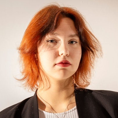 Katharina Zenses
ist im Porträt zu sehen. Sie hat gestuftes rotes Haar und blickt in ernst die Kamera.