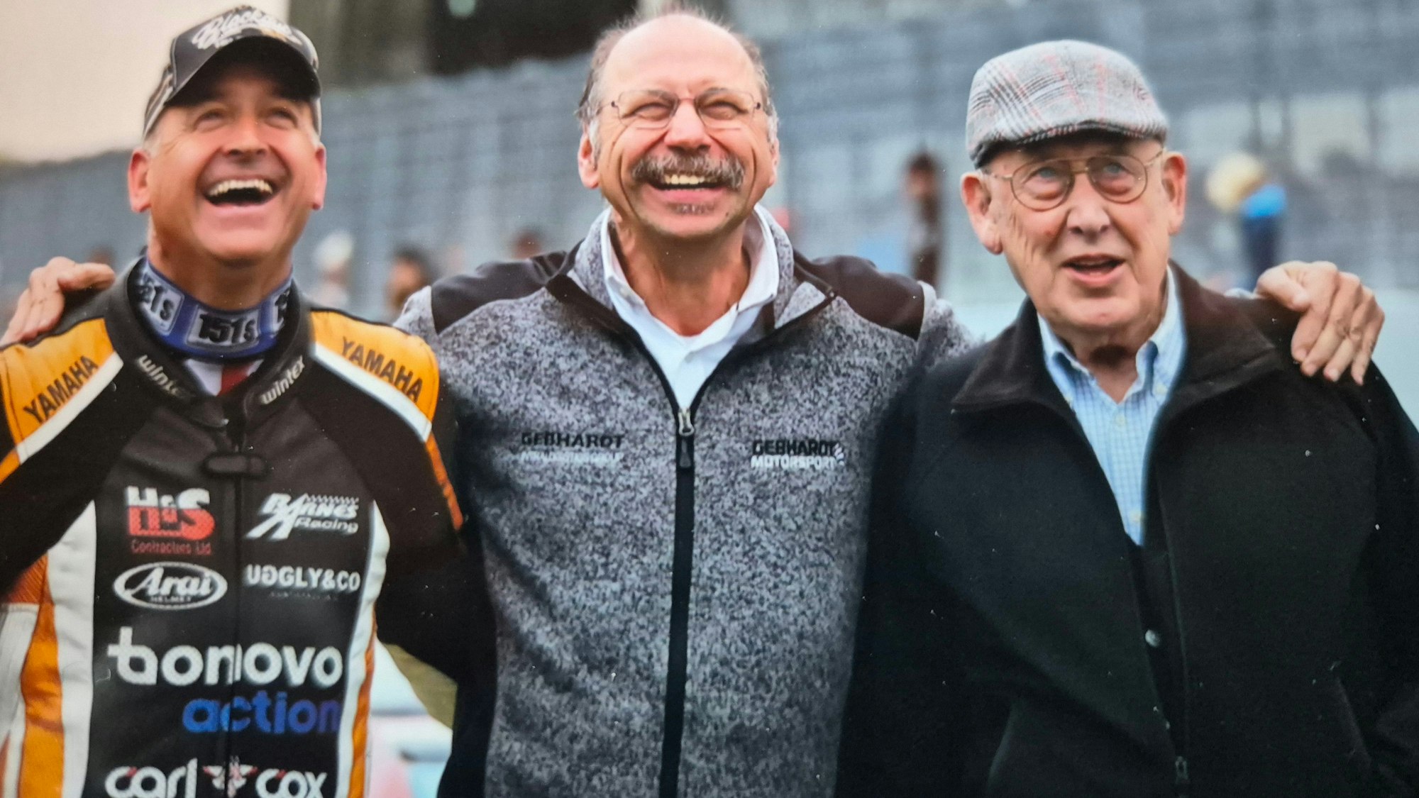 Zu sehen sind drei Motorsportler, die sich umarmen.