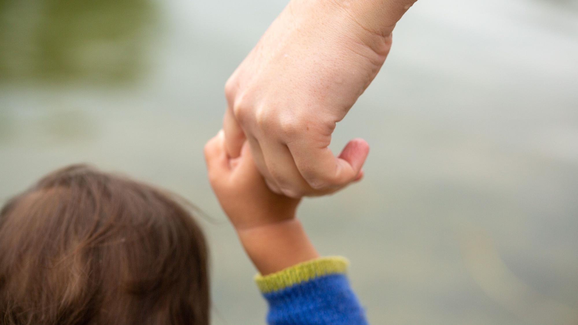 Ein Kind hält die Hand eines Erwachsenen.