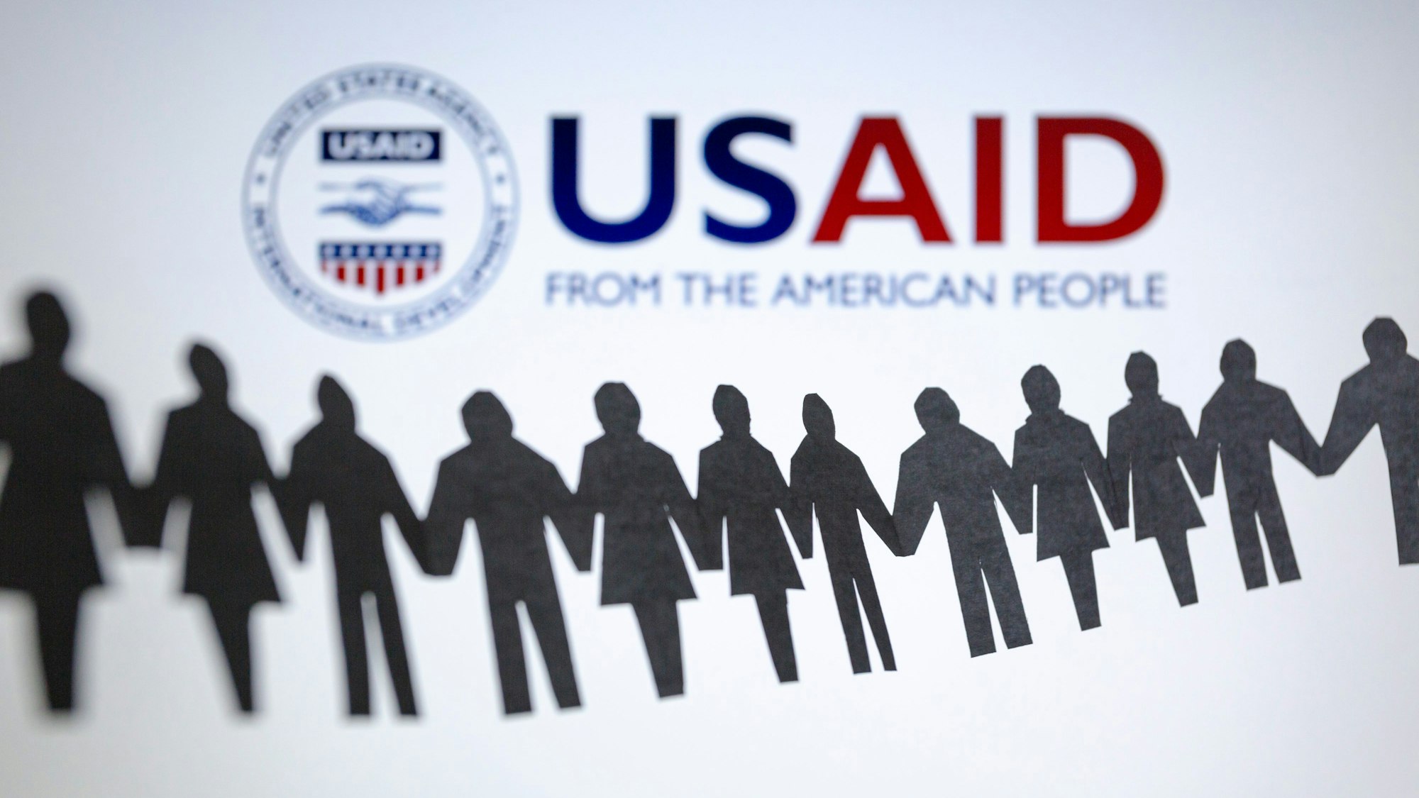 Das Logo der US-Entwicklungsbehörde, United States Agency for International Development (USAID), ist hinter einer Kette von ausgeschnittenen Papierfiguren zu sehen.