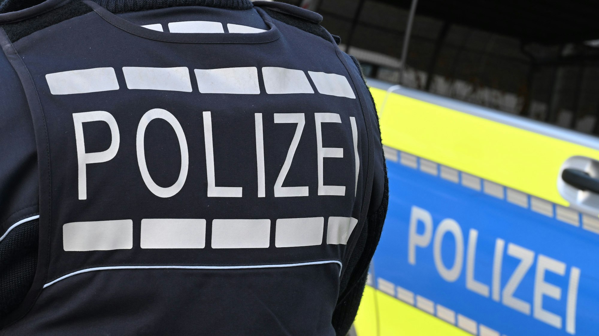 Auf dem Foto ist ein Beamter in Polizeiuniform und ein Streifenwagen.