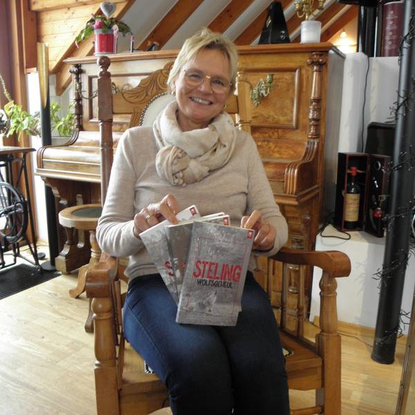Ute Mainz sitzt in einem Stuhl und hält ihr neues Buch in Händen, im Hintergrund ist ein Klavier zu sehen.