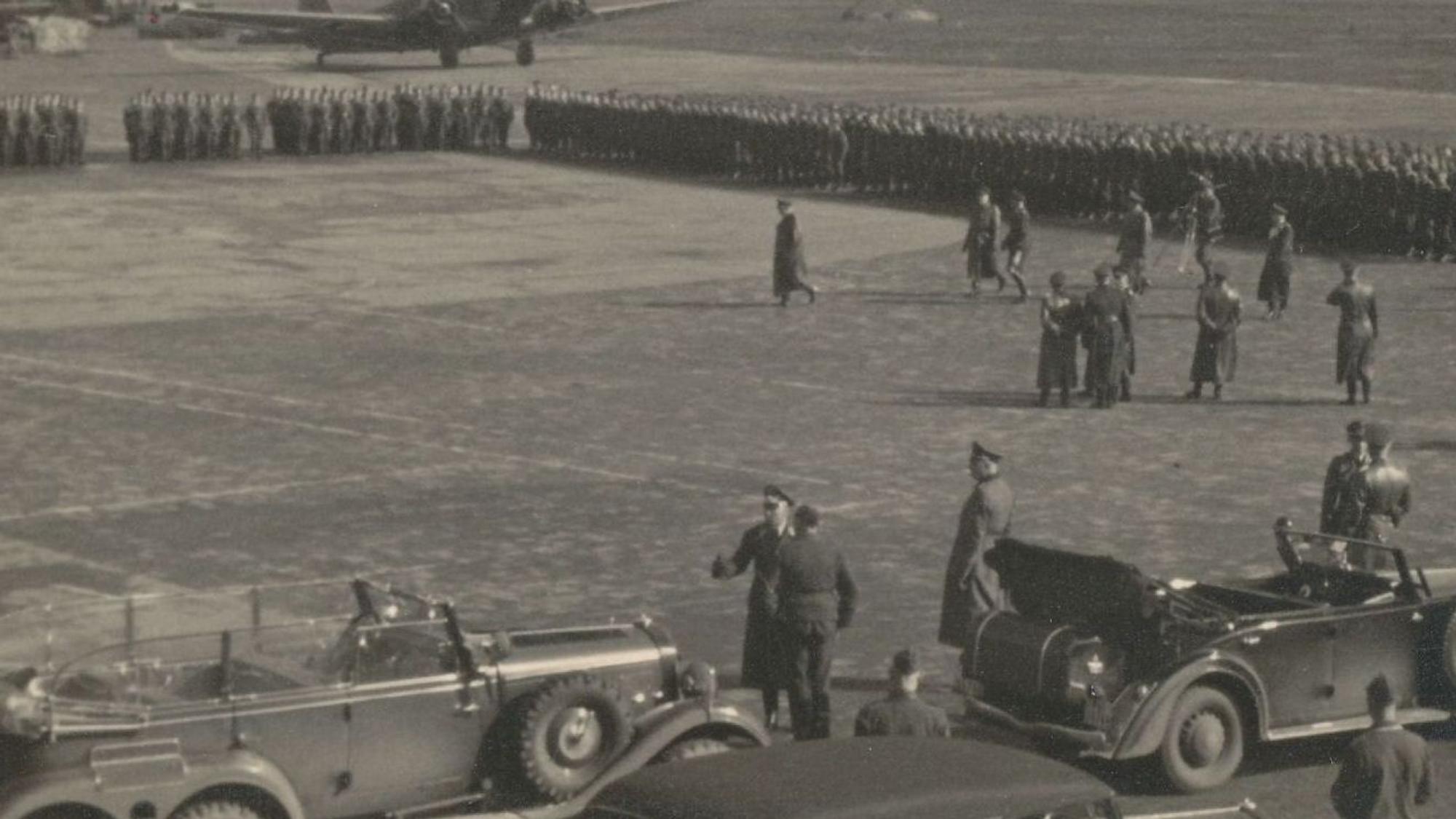 Zu sehen ist ein Schwarzweißfoto, auf dem die Spitze der Luftwaffe den Fliegerhorst Ostheim besucht. Im Hintergrund ist eine große Ansammlung von Soldaten zu sehen.