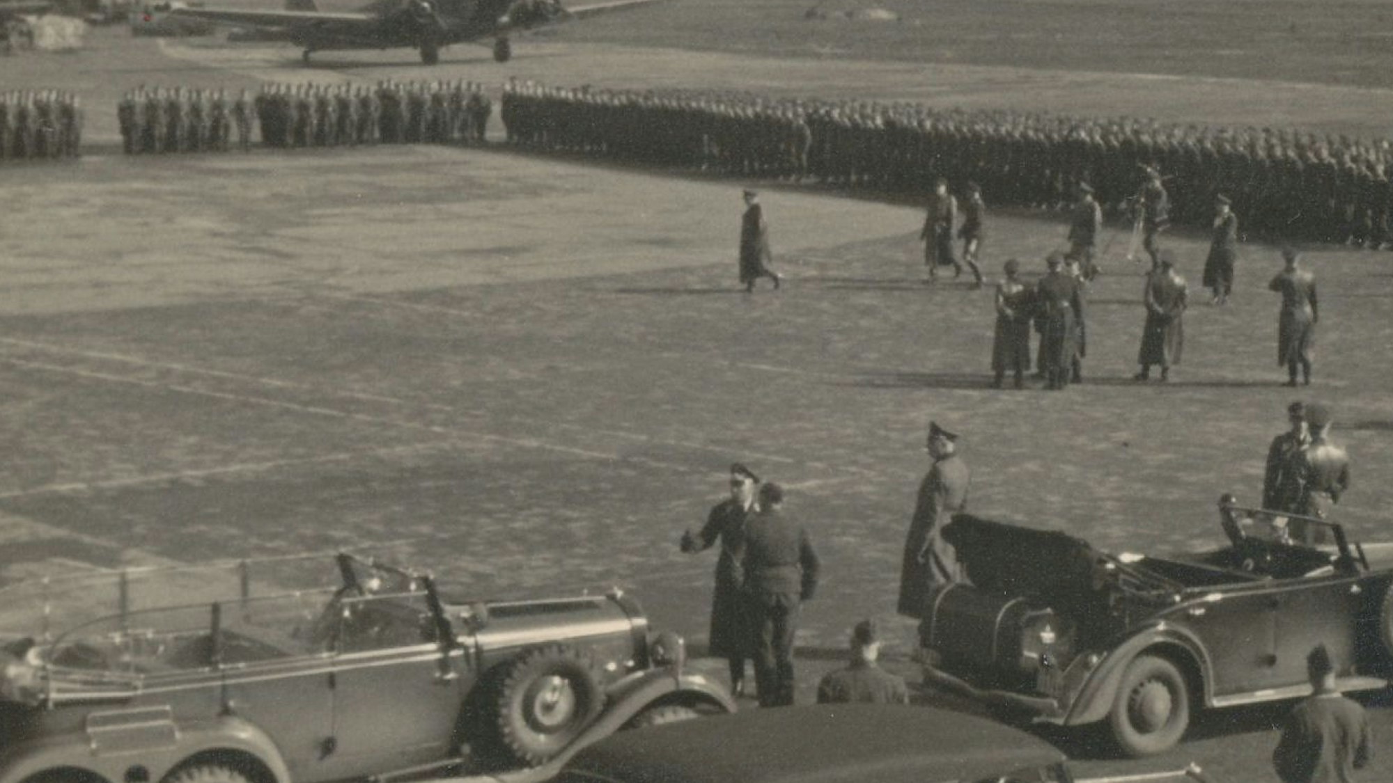 Zu sehen ist ein Schwarzweißfoto, auf dem die Spitze der Luftwaffe den Fliegerhorst Ostheim besucht. Im Hintergrund ist eine große Ansammlung von Soldaten zu sehen.