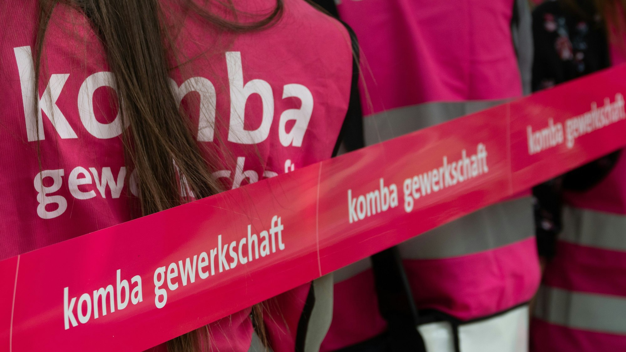 Demonstranten stehen hinter einem pinken Flatterband mit der Aufschrift „komba gewerkschaft“.