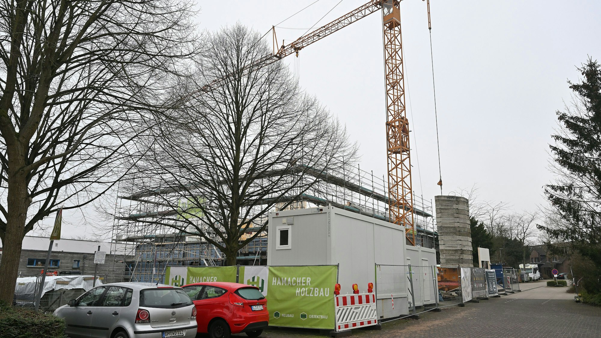 Ein großer gelber Baukran ragt über den eingezäunten Rohbau.