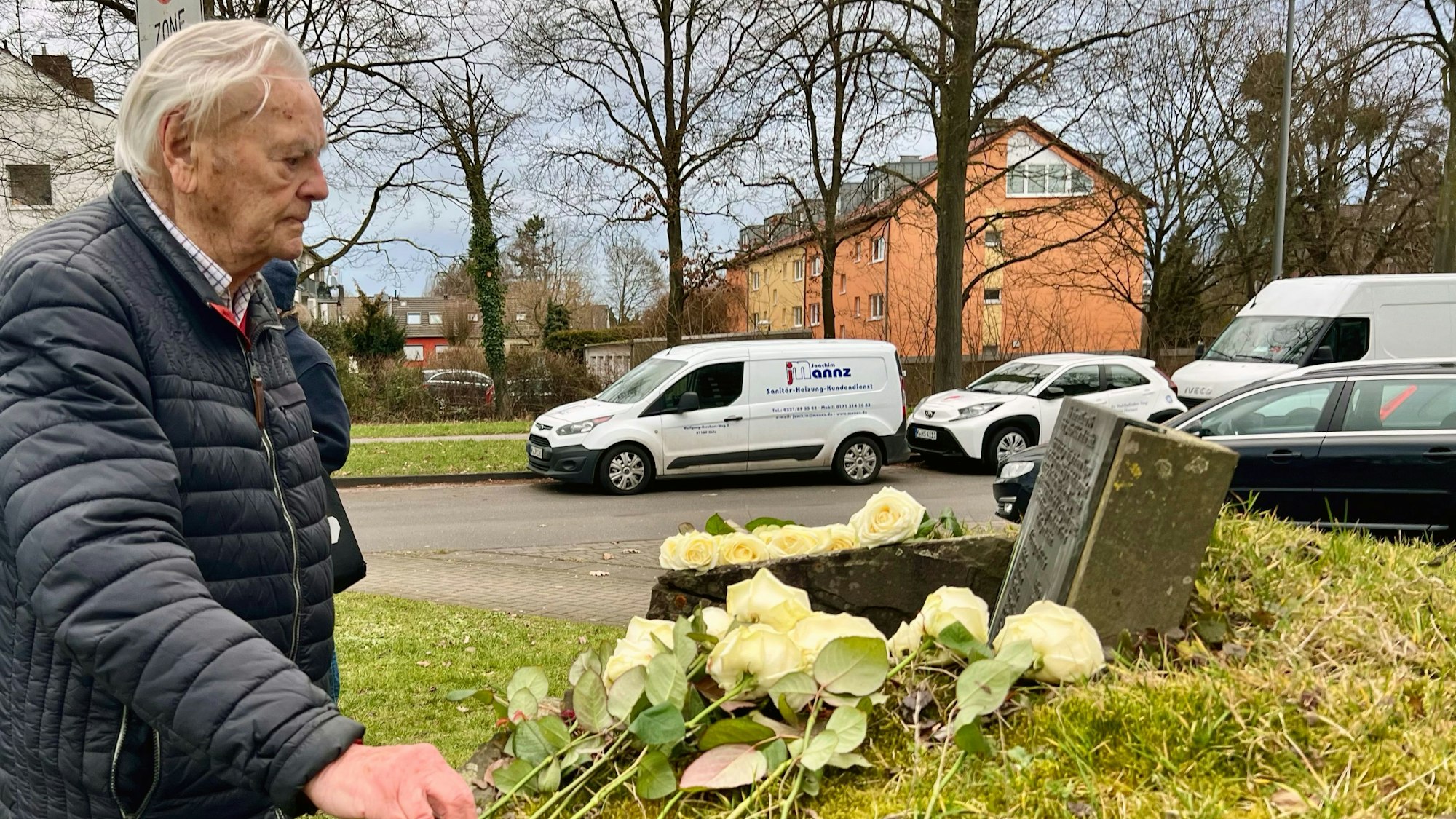 Ein alter Mann legt eine weiße Rose zu anderen Rosen auf einem Gedenkstein.