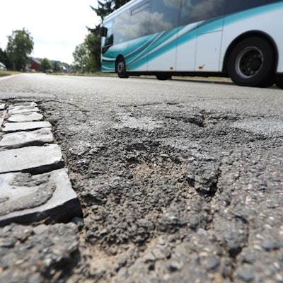 Schlaglöcher auf einer Straße, an denen gerade ein Linienbus vorbeifährt.