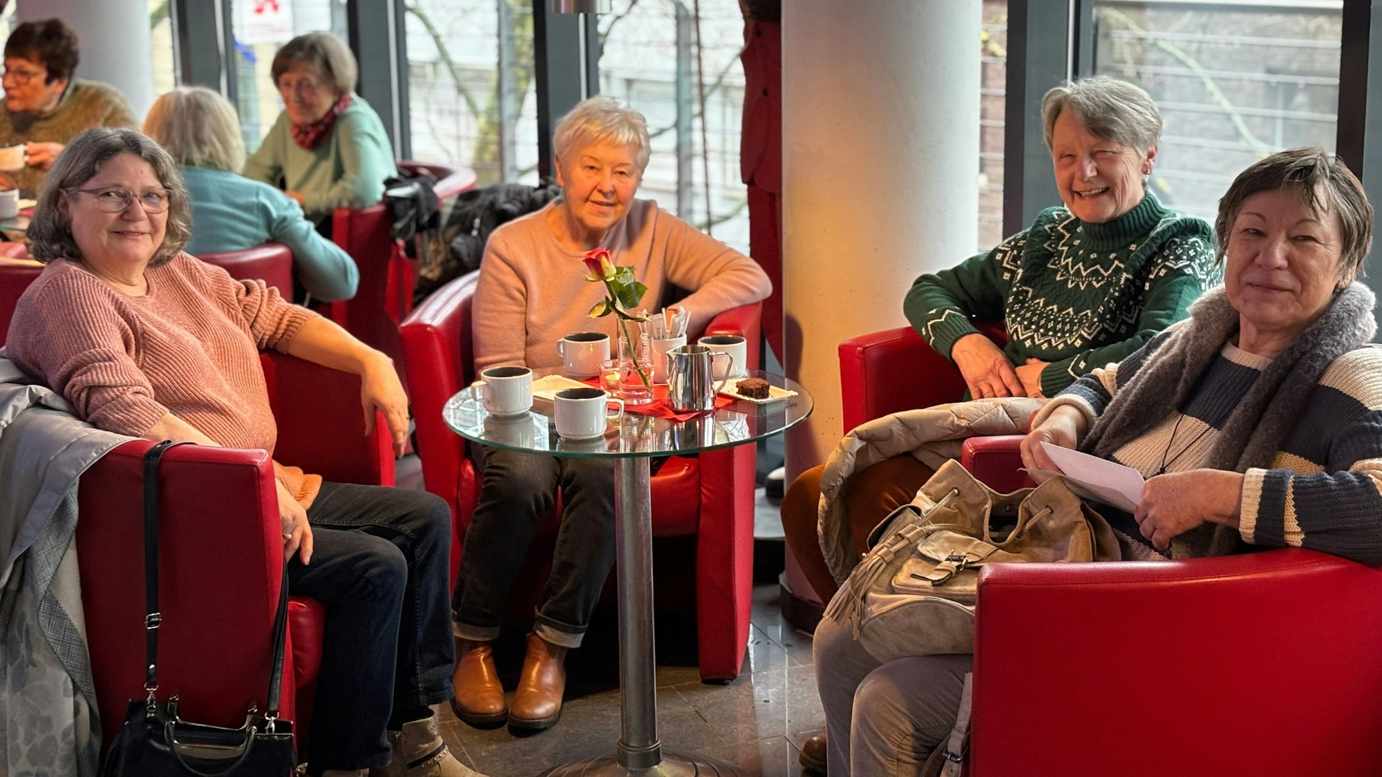 Vier Seniorinnen sitzen in Sesseln um einen Tisch, auf dem gefüllte Kaffeetassen stehen.