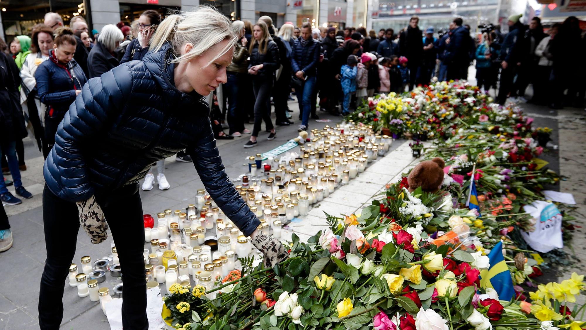 Eine Frau legt in Stockholm Blumen am Einkaufszentrum Ahlens nieder.