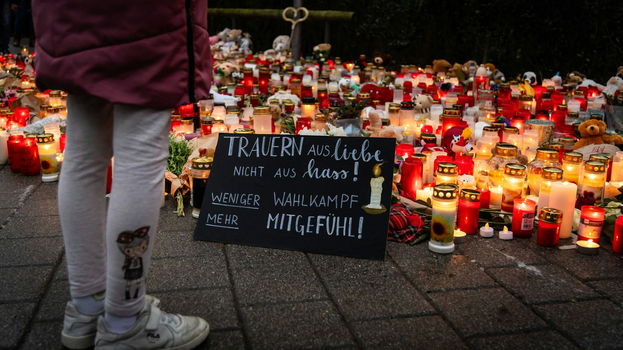 Ein Kind steht an einer Gedenkstätte in Aschaffenburg. Auf einem Schild steht „weniger Wahlkampf, mehr Mitgefühl“. (Archivbild)