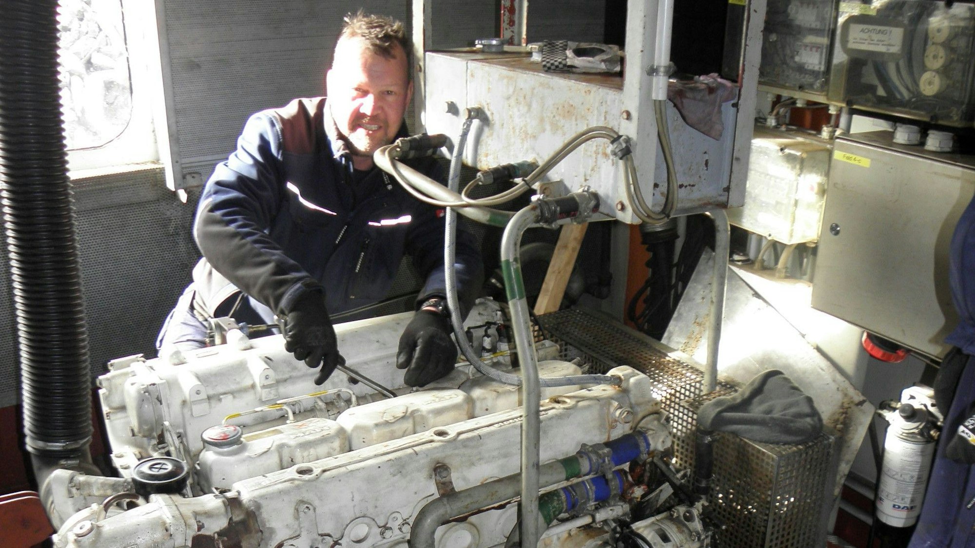 Ein Mann in Arbeitskleidung und Handschuhen ist im Maschinenraum des Rurseeschiffs Aachen und schraubt am Motor.