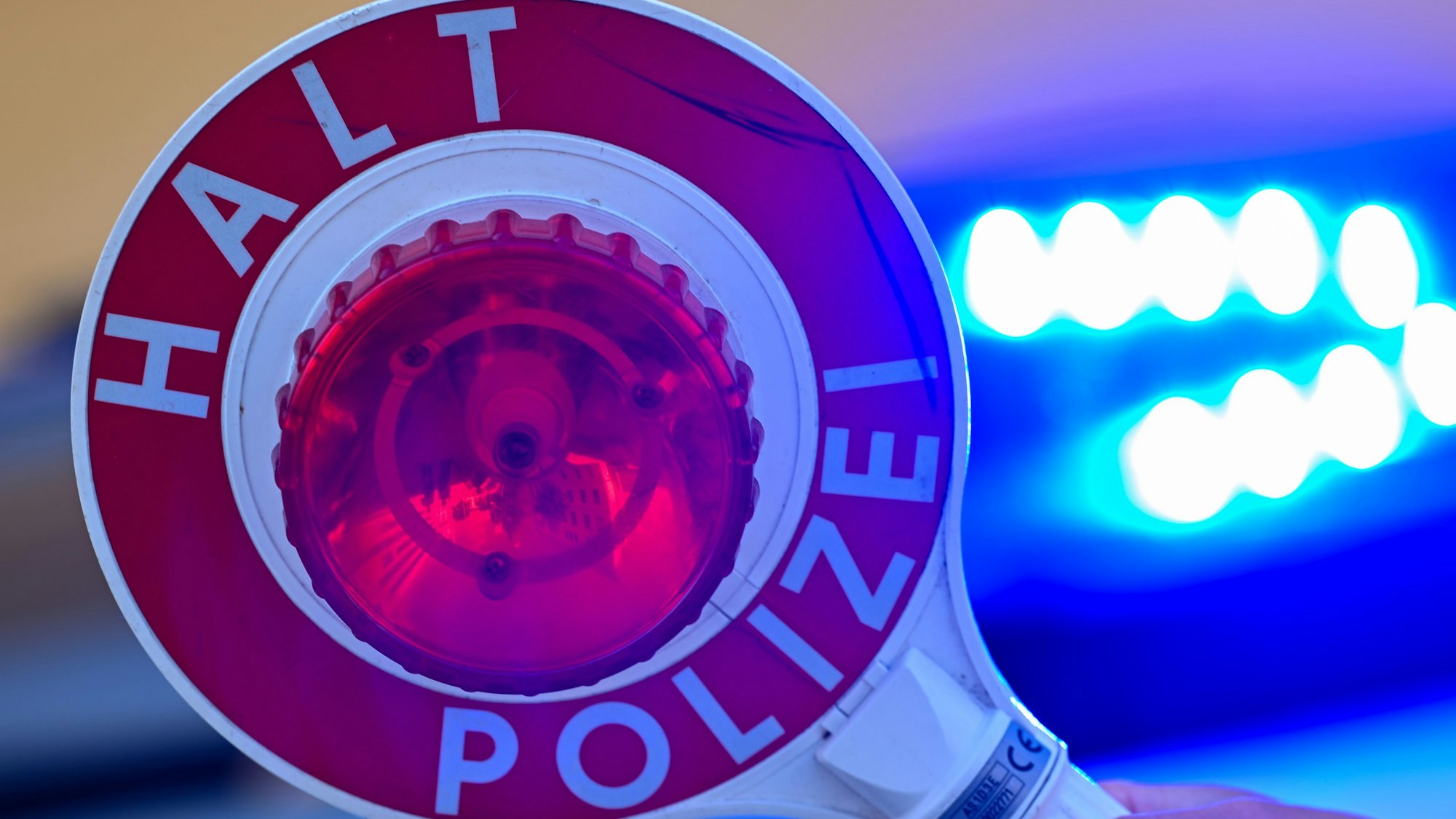 Eine Kelle der Polizei mit der Aufschrift Halt Polizei vor einem Blaulicht eines Polizeifahrzeuges