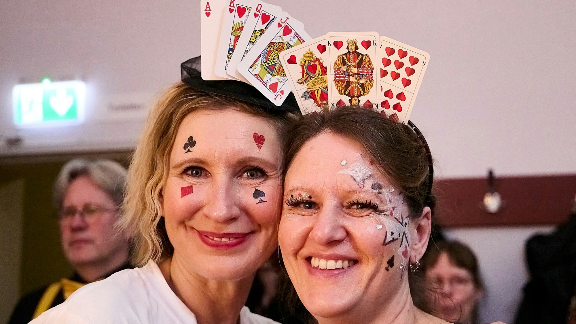 Zwei Besucherinnen haben sich aus Spielkarten Kopfbedeckungen gebastelt. Im Gesicht Symbole von Herz, Karo, Pik und Kreuz.
