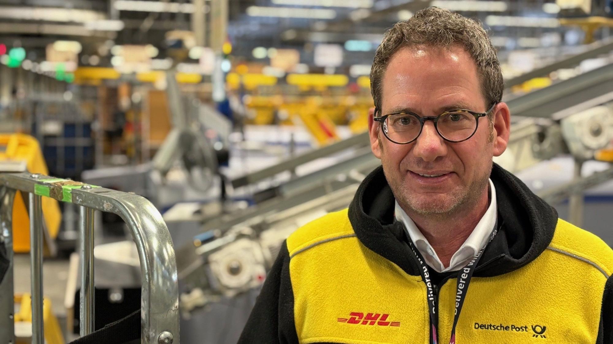 Auf dem Bild ist der neue Leiter der DHL-Niederlassung Betrieb Köln-West in einem Verteilzentrum zu sehen.