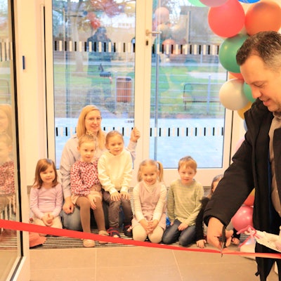 Sacha Reichelt schneidet ein rotes Band durch. Mehrere Kinder und eine Erzieherin im Hintergrund schauen zu.