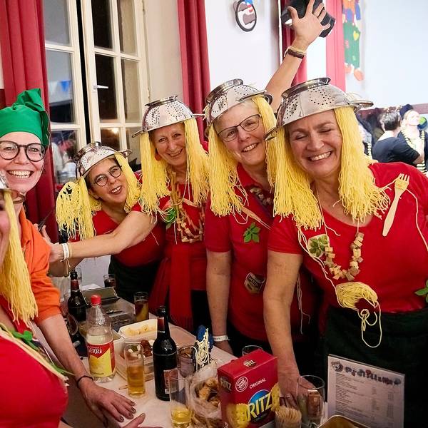 Eine Gruppe Frauen hat sich lustige Kostüme gebastelt: Zum tomatenroten Shirt tragen sie Nudelsiebe auf dem Kopf, die daran befestigten Fäden sehen aus wie Spaghetti.