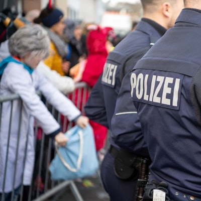 Das Bild zeigt zwei Polizisten beim Rosenmontagszug in Euskirchen. Im Hintergrund stehen einige Jecke.