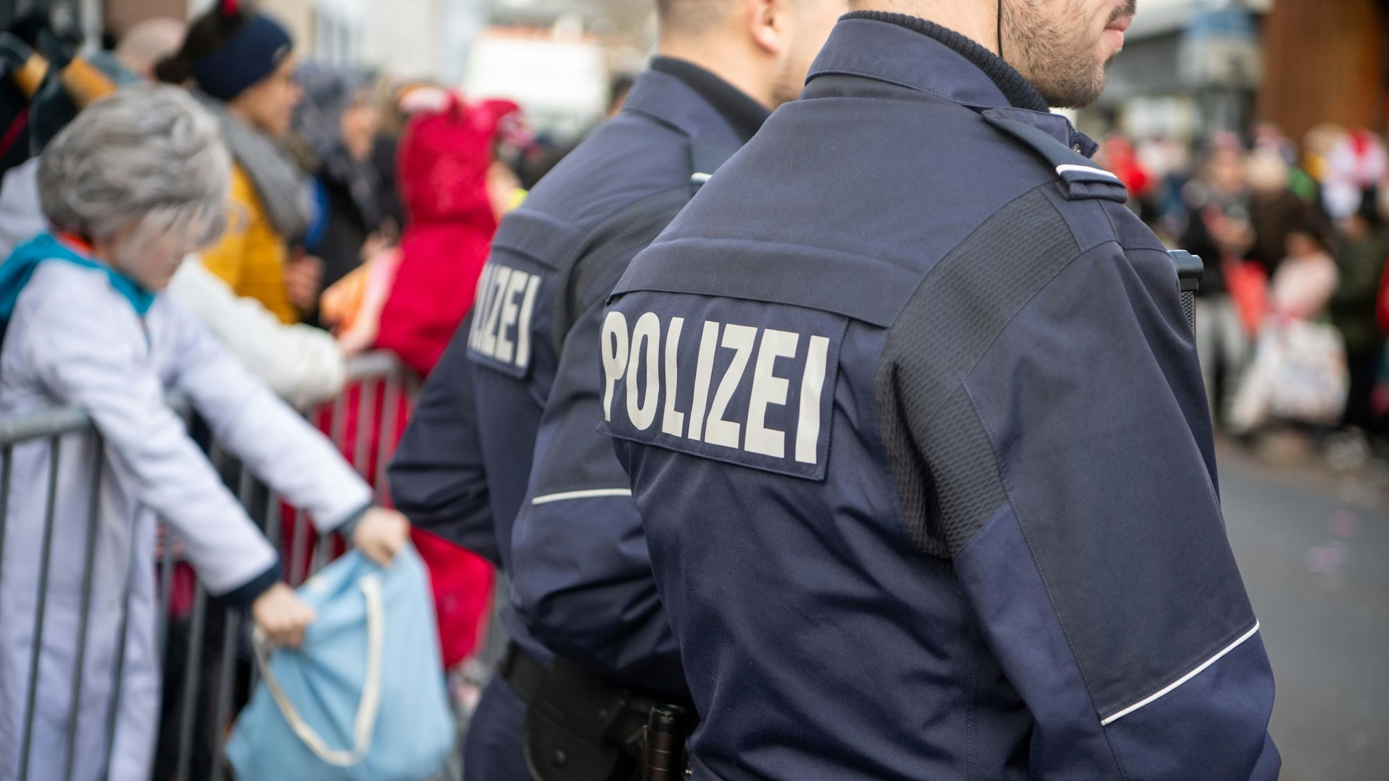 Das Bild zeigt zwei Polizisten beim Rosenmontagszug in Euskirchen. Im Hintergrund stehen einige Jecke.