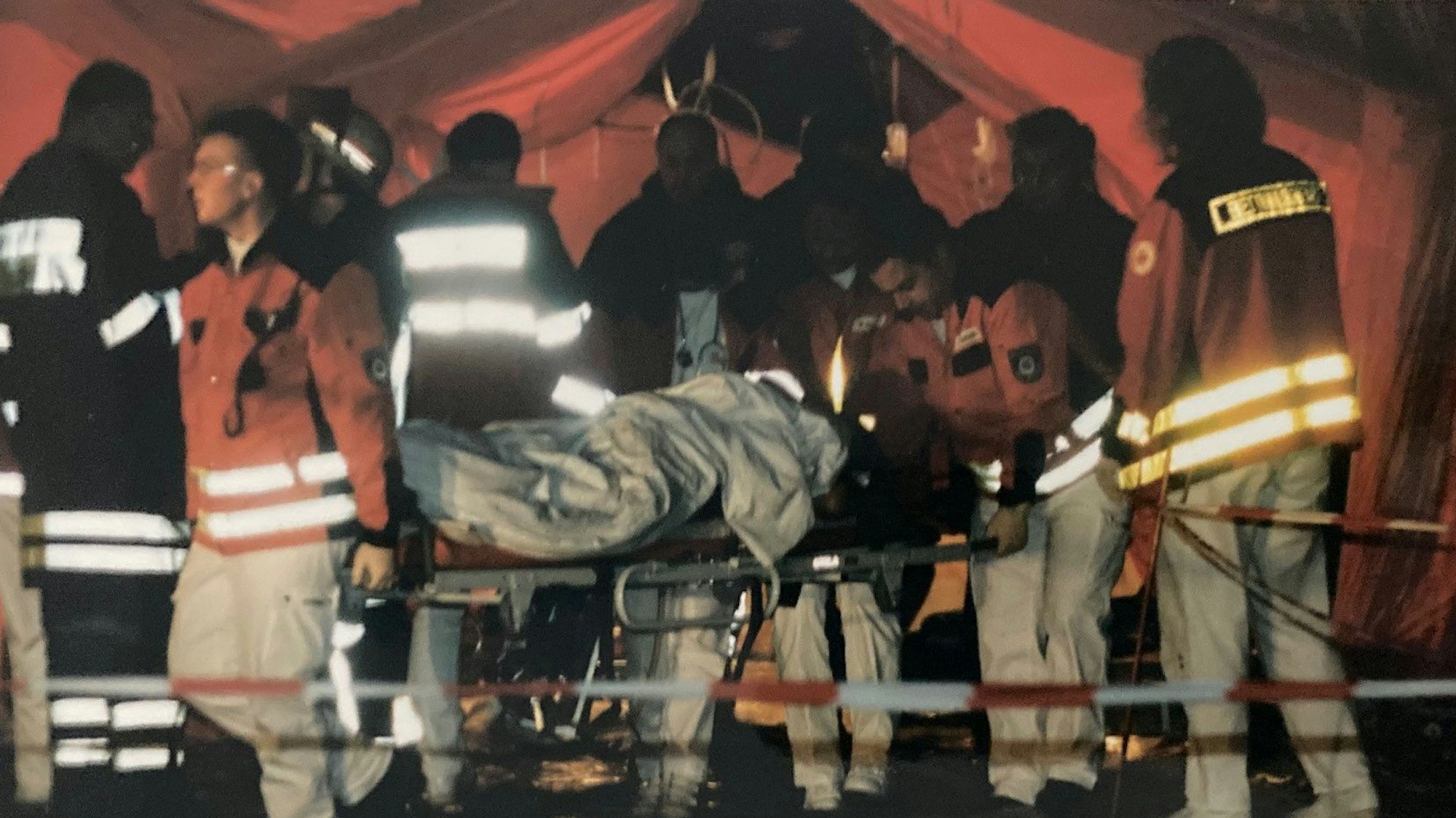 Das Bild zeigt Einsatzkräfte, die einen Verletzten auf der Trage in ein Zelt bringen.