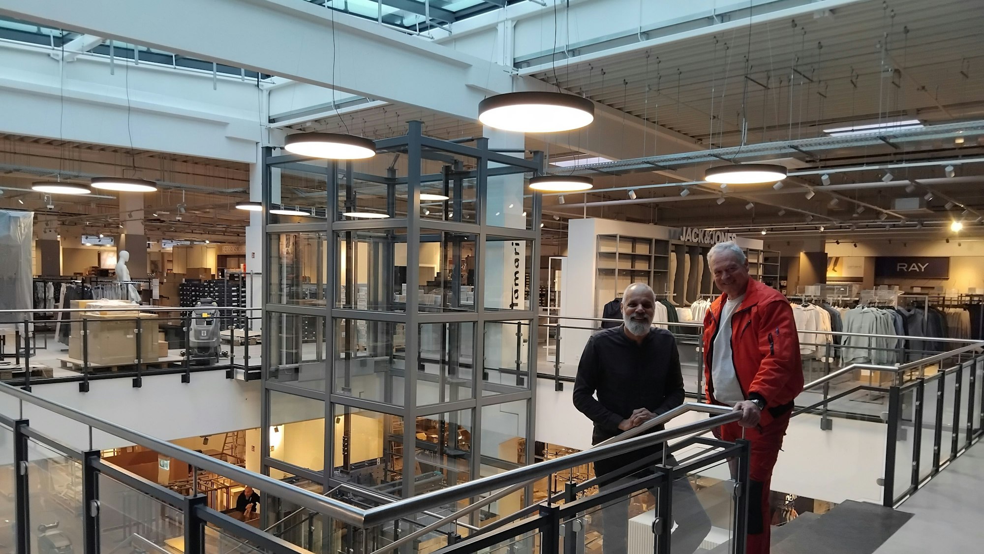 Zwei Männer stehen an einer Treppe in einem Kaufhaus