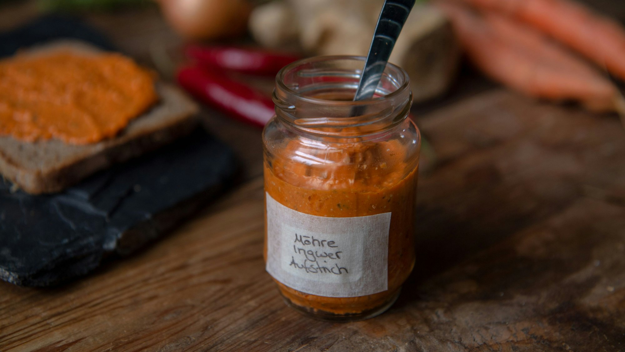 Ein Brotaufstrich im Weckglas, dahinter ein Brot mit Aufstrich darauf.