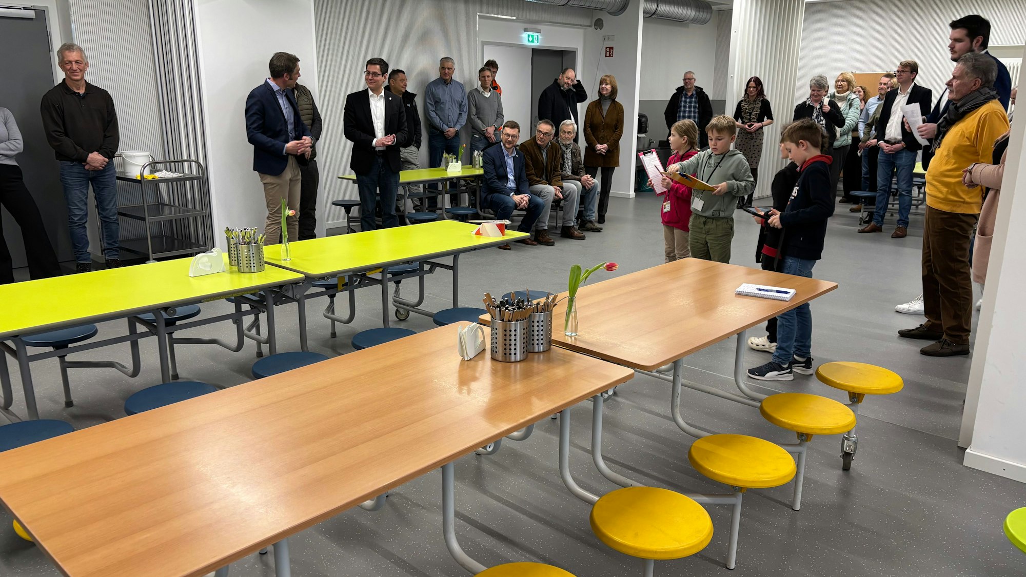 Auf einer Nahaufnahme hält eine Hand eine durchsichtige Greifzange, die Mäusespeck in Form einer Maus aus einer Schale mit Süßigkeiten gepackt hat.