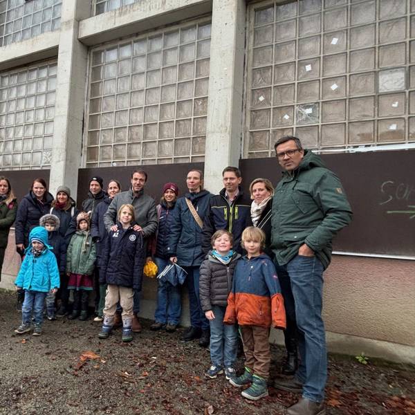 Auf dem Bild ist eine Gruppe von Eltern mit ihrem Kindern vor einer alten Sporthalle zu sehen.
