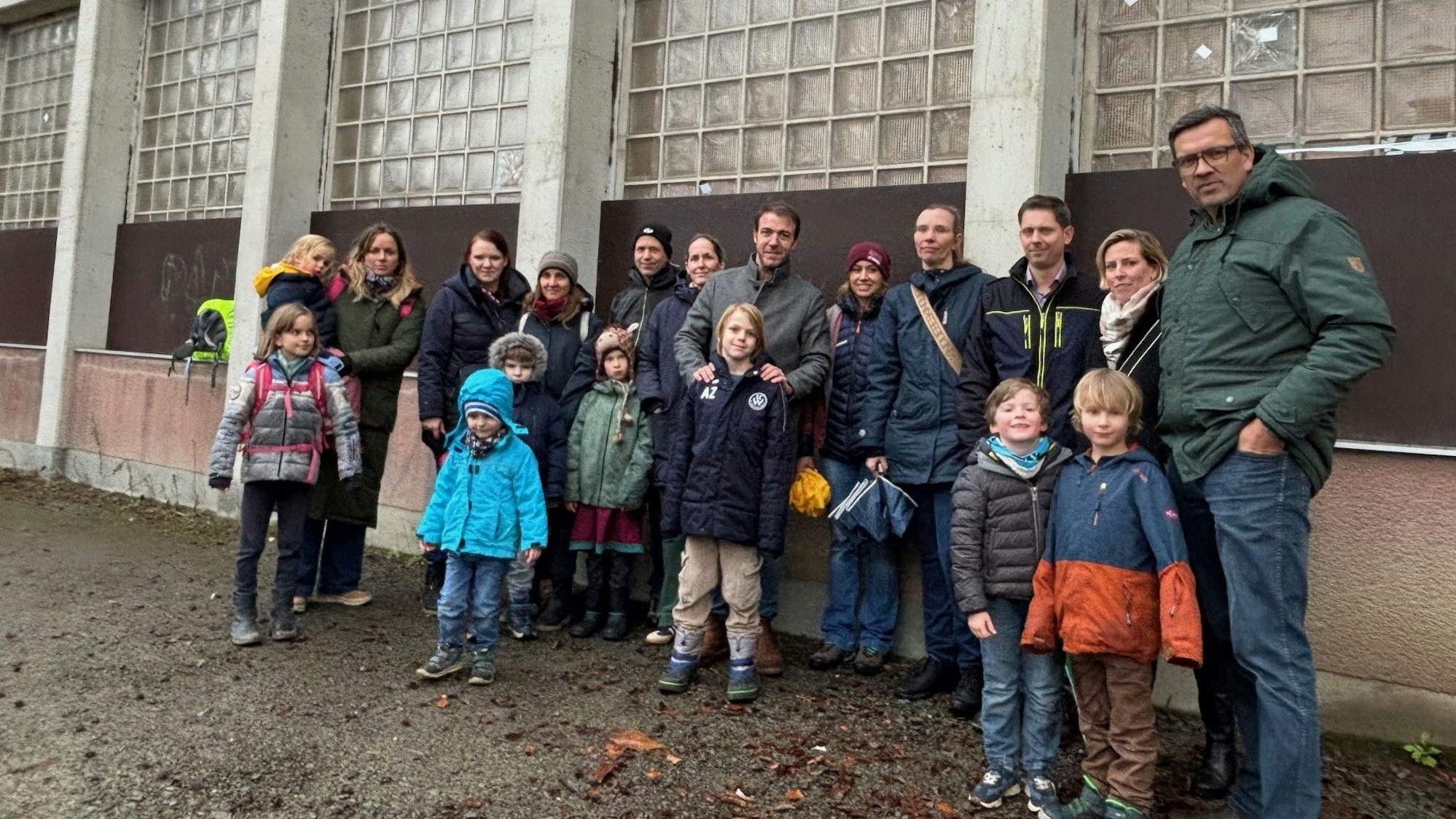Auf dem Bild ist eine Gruppe von Eltern mit ihrem Kindern vor einer alten Sporthalle zu sehen.