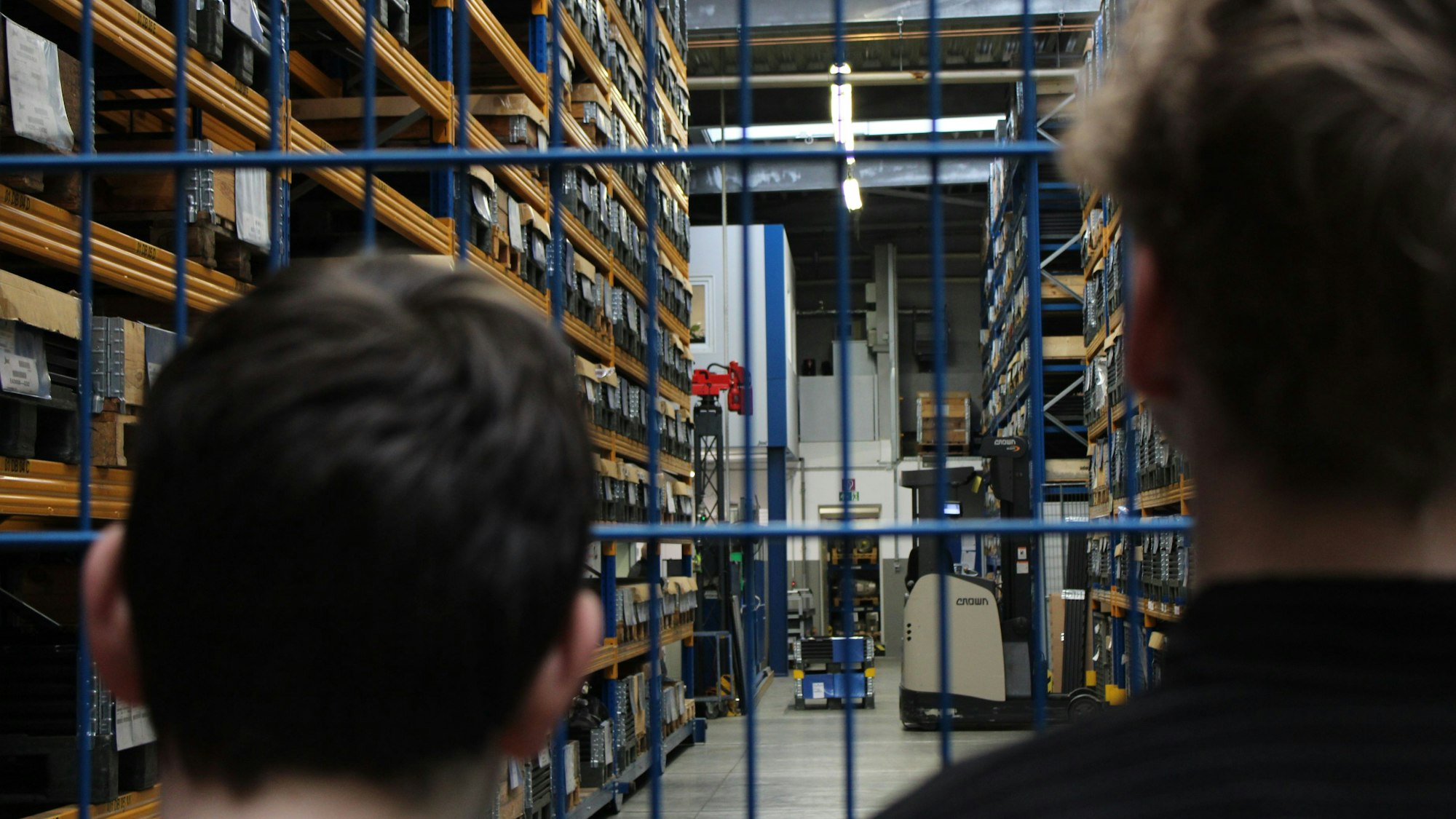 Zwei Jungen sind von hinten zu sehen, wie sie in das Lager einer Maschinenfabrik schauen.