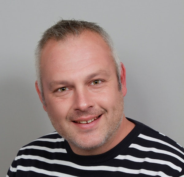 Ein Mann und eine Frau halten mehrere Geldscheine vor einem Kindergarten in den Händen.