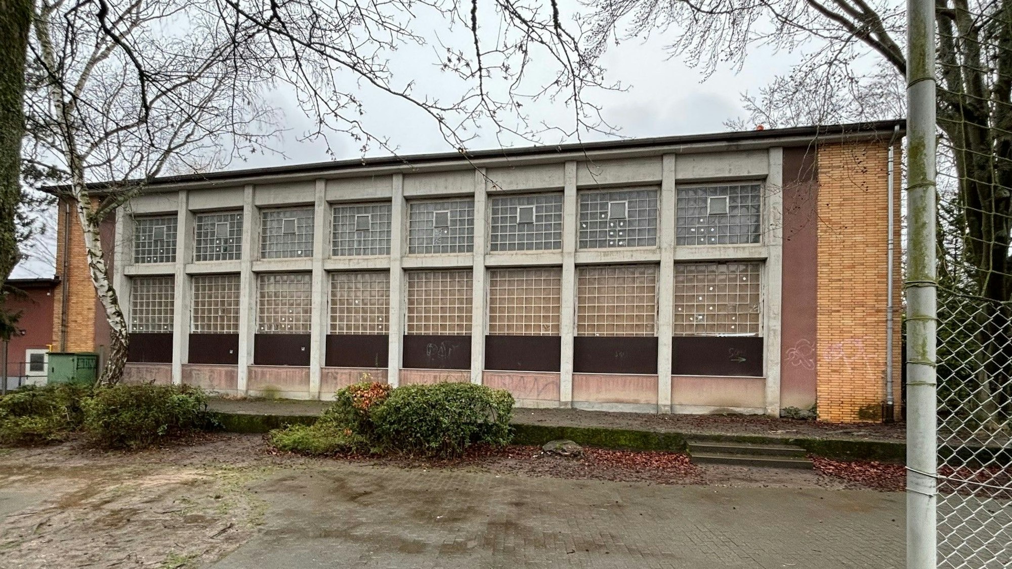 Das Foto zeigt eine alte Sporthalle, de unteren Fensterreihen sind mit Spanplatten gesichert.