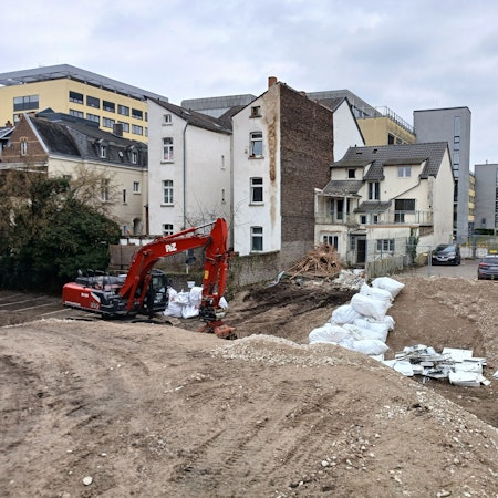 Ein Bagger vor einem Graben und einer Häuserzeile.