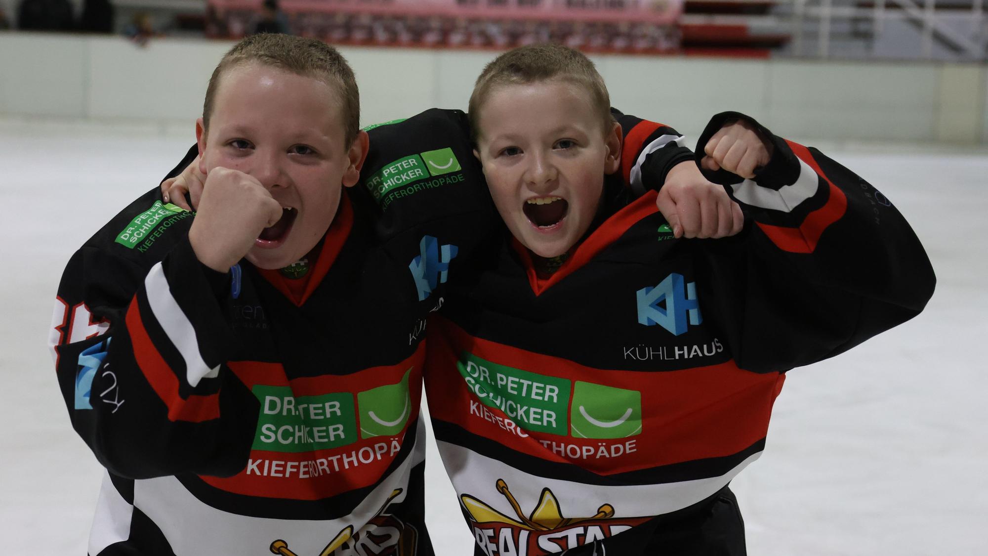 Die Zwillinge Finn und Florian Wolf aus Satzvey tragen Eishockey-Trikots. Mit geballten Fäusten jubeln sie über einen Sieg.