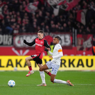 Das Bild zeigt einen Zweikampf zwischen Florian Wirtz und Kevin Akpoguma.