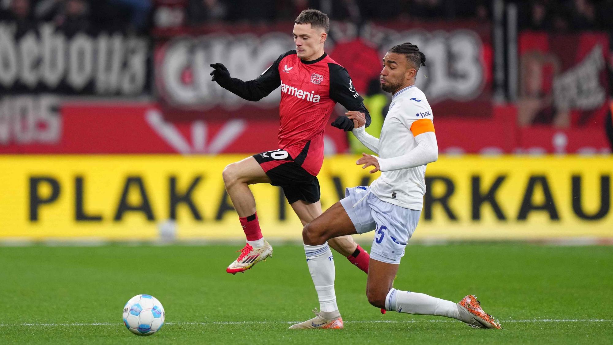 Das Bild zeigt einen Zweikampf zwischen Florian Wirtz und Kevin Akpoguma.