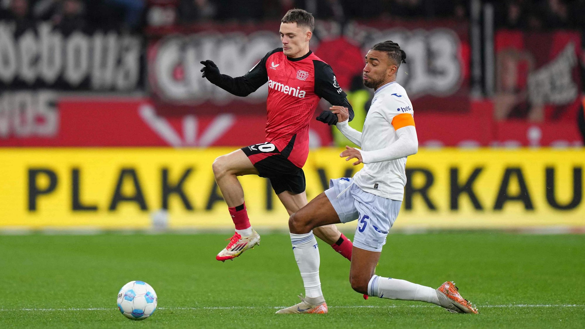 Das Bild zeigt einen Zweikampf zwischen Florian Wirtz und Kevin Akpoguma.