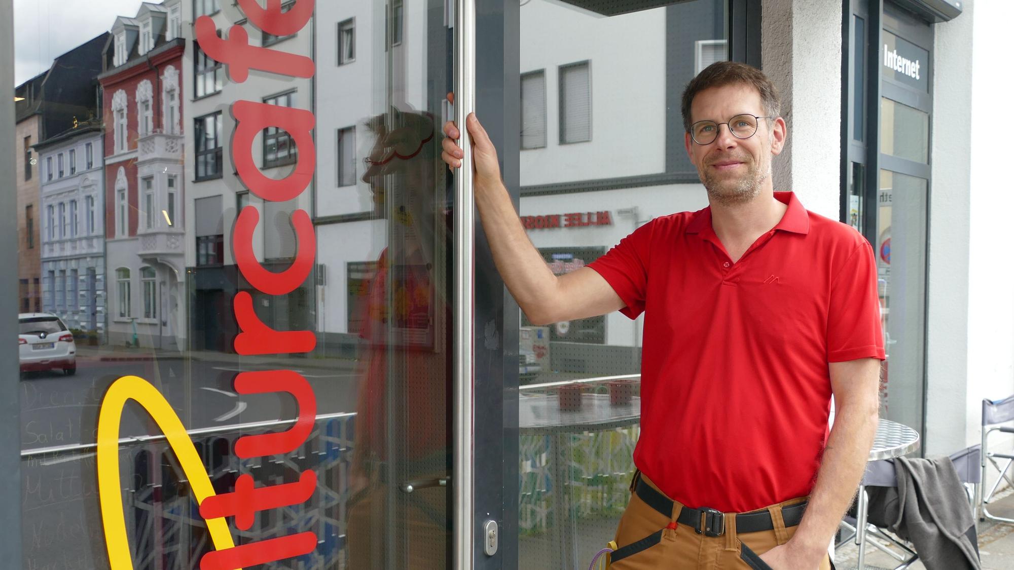 Ein Mann steht neben einer Tür, auf der abgeschnitten „Kulturcafé“ zu lesen ist.