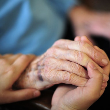 Eine Pflegekraft hält in einem Seniorenheim die Hand einer Bewohnerin.