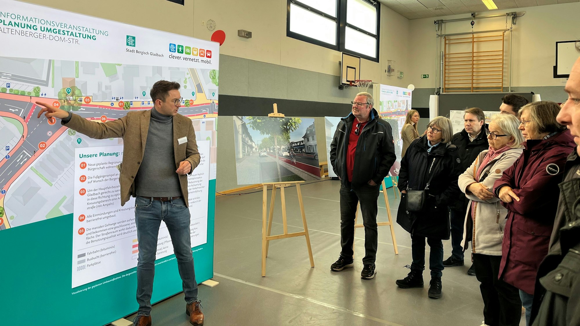 Der Planer steht vor einer Stellwand. Besucher hören ihm zu.