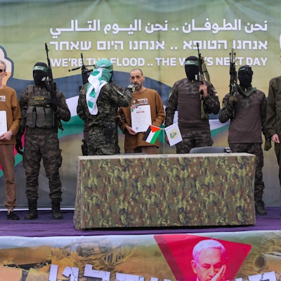 Palestinian Hamas fighters escort(L-R) Ohad Ben Ami, Or Levy and Eli Sharabi on a stage before handing them over to a Red Cross team in Deir el-Balah, central Gaza, on February 8, 2025, as part of the fifth hostage-prisoner exchange of a fragile ceasefire. The swap comes after US President Donald Trump proposed clearing out the Gaza Strip of its inhabitants and for the United States to take over the Palestinian territory -- a plan that has sparked global uproar and been rejected by Hamas. (Photo by Eyad BABA / AFP)
