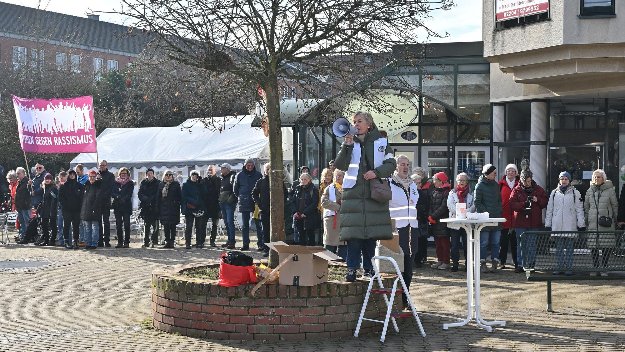 Vor einer langen Menschenkette, die ein Schild mit der Aufschrift „Aufstehen gegen Rassismus“ hochhält, spricht eine Frau in ein Mikrofon.