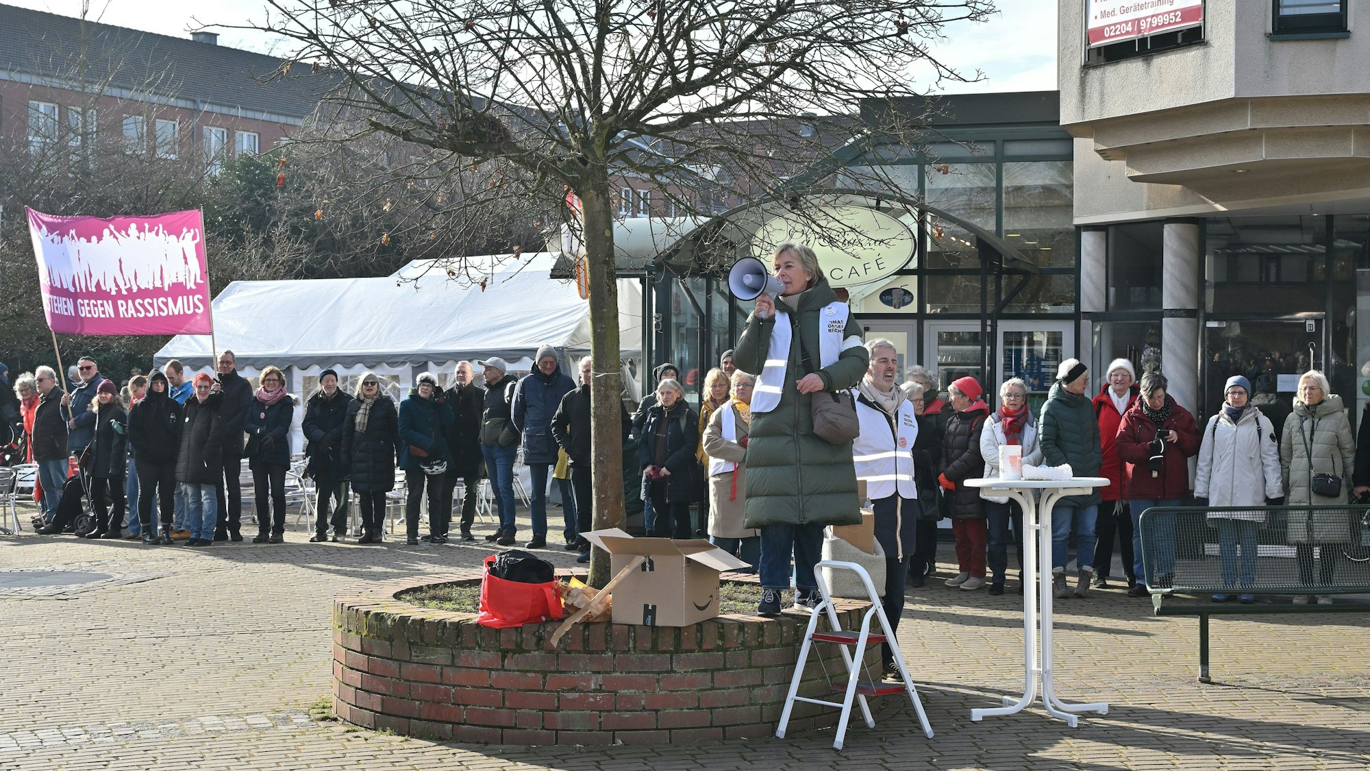 Vor einer langen Menschenkette, die ein Schild mit der Aufschrift „Aufstehen gegen Rassismus“ hochhält, spricht eine Frau in ein Mikrofon.