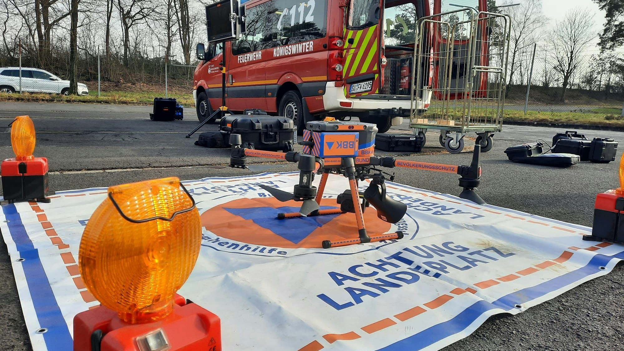 Eine Drohne steht auf einer Plane mit der Aufschrift „Achtung Landeplatz“.
