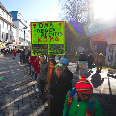 Das Foto zeigt eine Menschenkette, eine der Teilnehmerinnen hält ein Schild mit der Aufschrift "Oma gegen rechtes Koma".